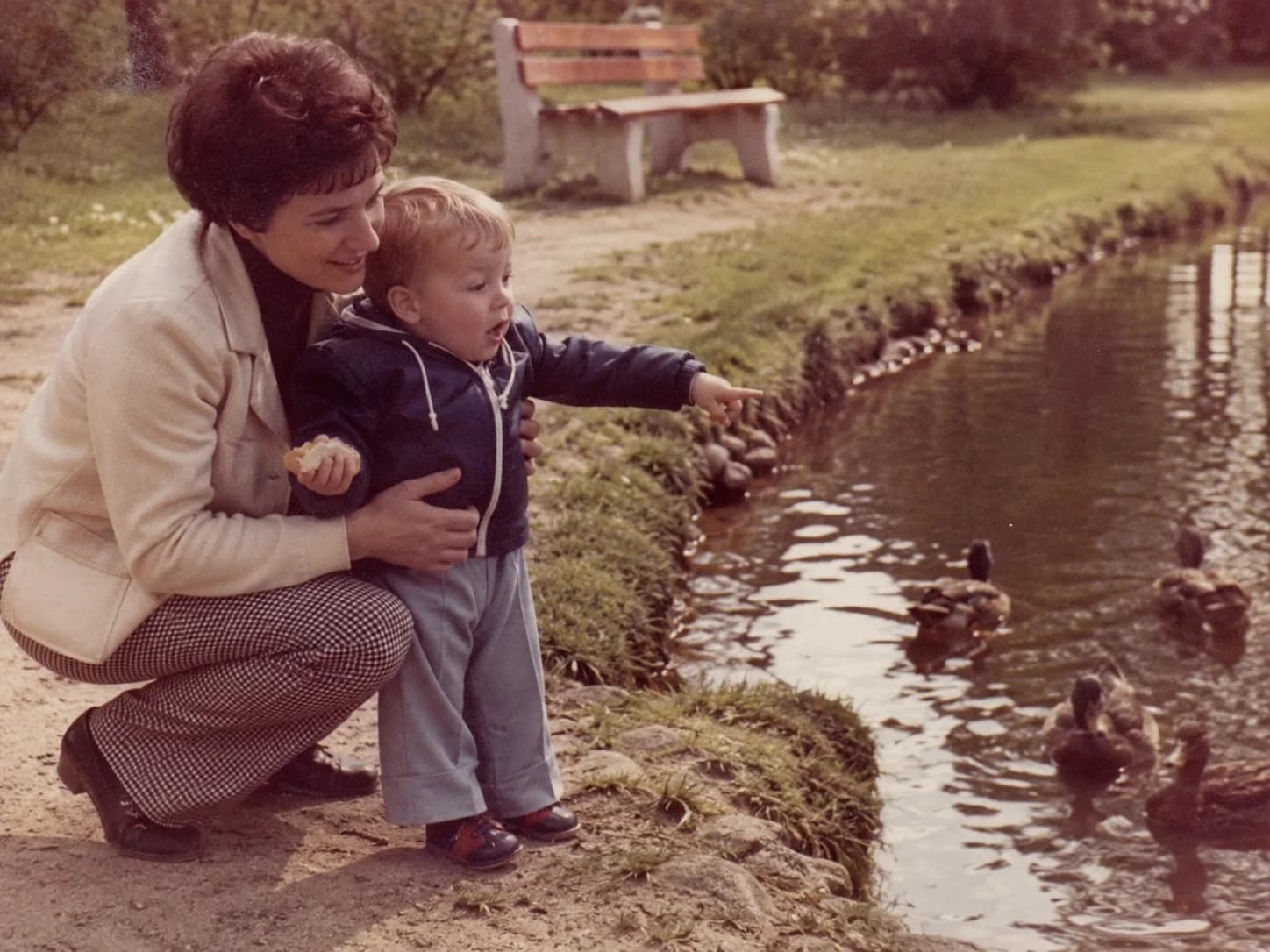 A mother and her small son feeding ducks at a pond