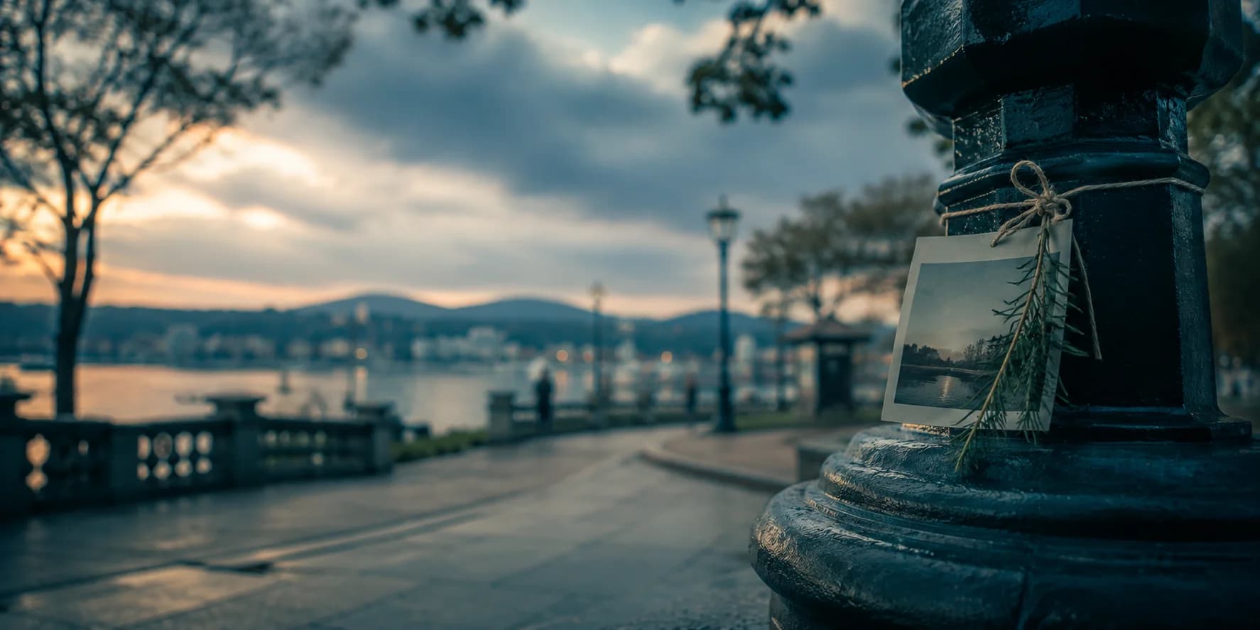 A photograph tied to a lamp post on a waterfront promenade at dusk